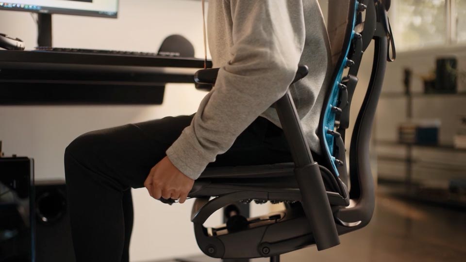 A close-up video of the side of a black Embody Gaming Chair adjustable seat depth mechanism being adjusted by a person in a sweatshirt and pants.
